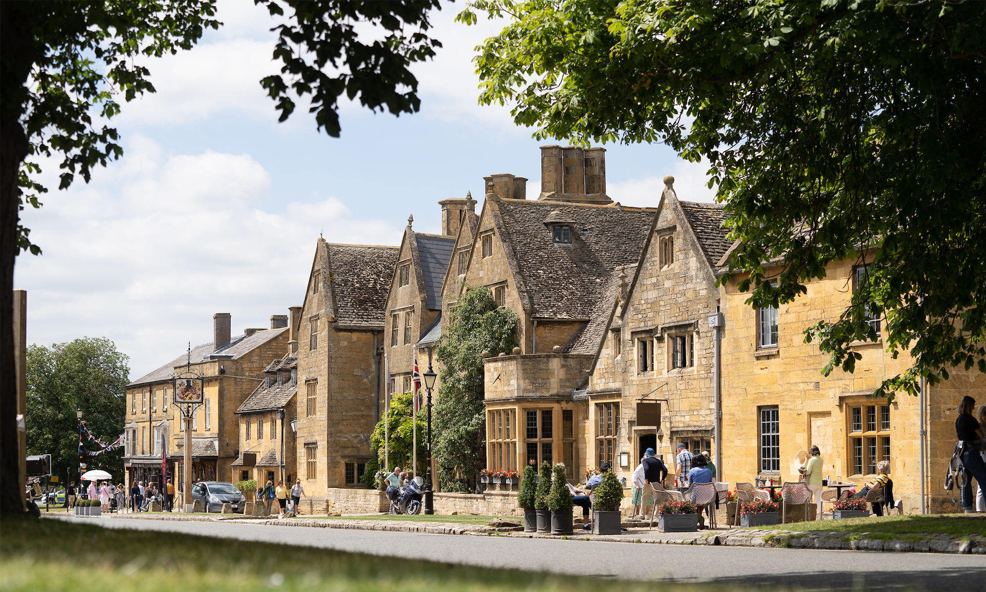 Facade of The Lygon Arms during the summer season, with green gardens and people strolling in front of the property