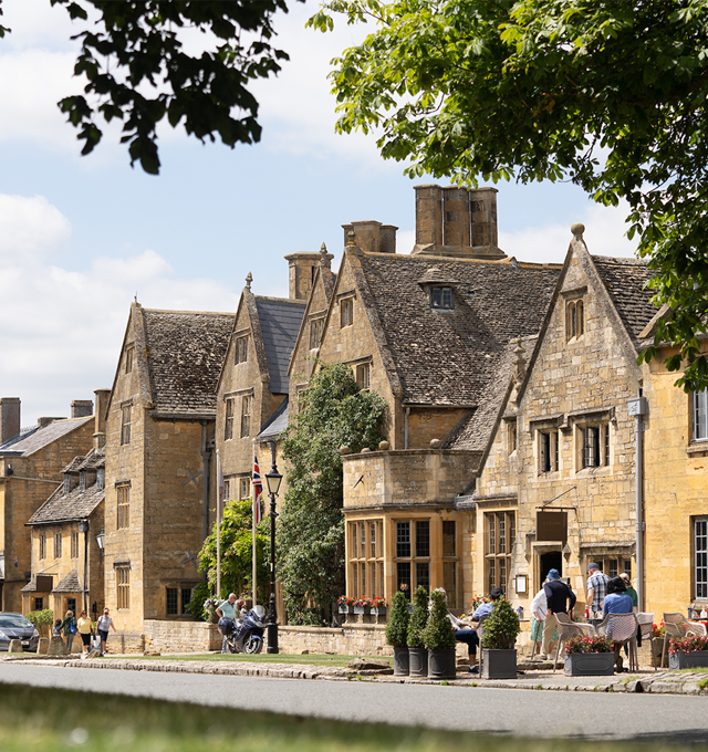 Facade of The Lygon Arms during the summer season, with green gardens and people strolling in front of the property