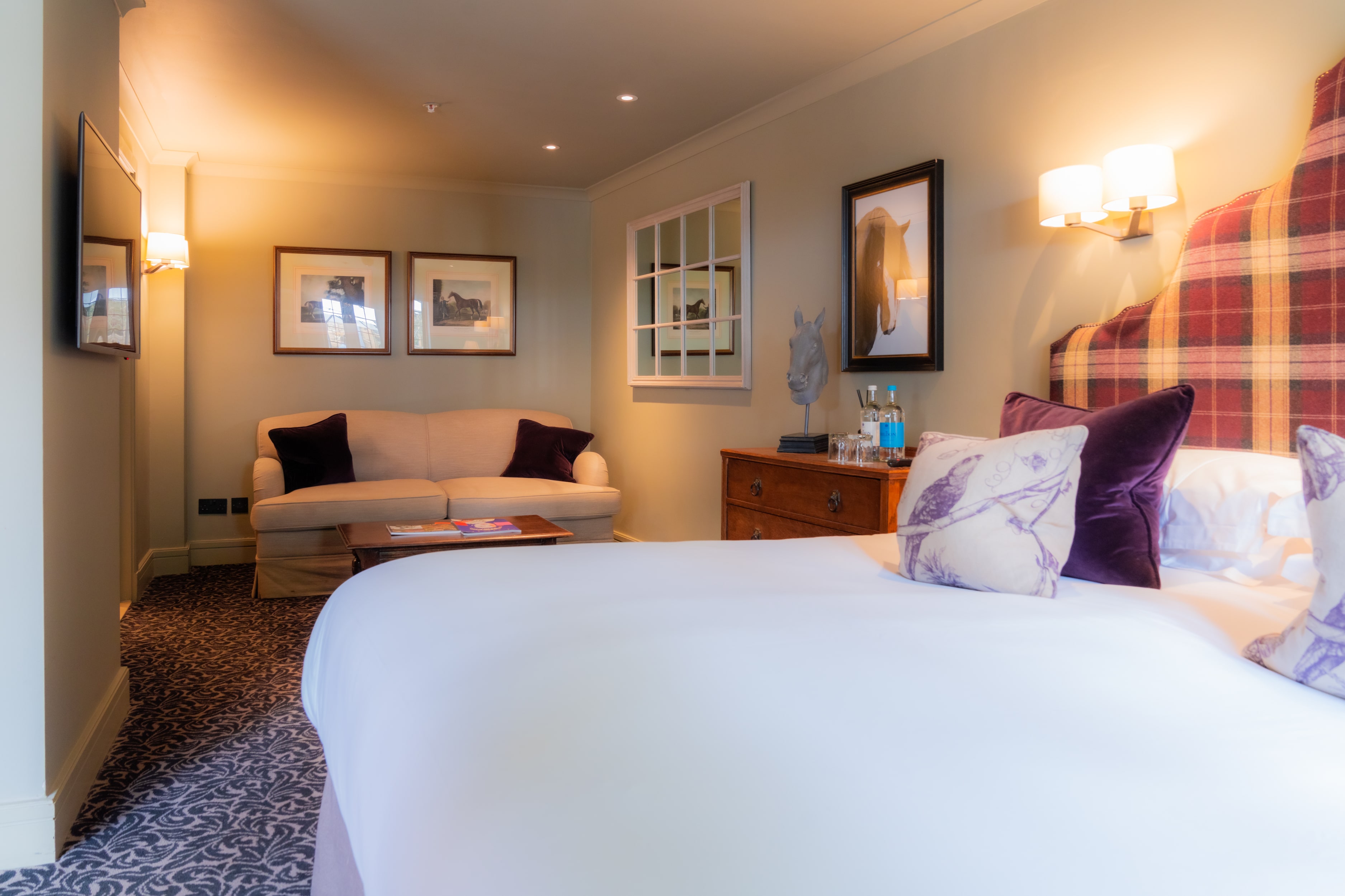 A bright hotel bedroom with a plaid headboard and mirrored wardrobe.