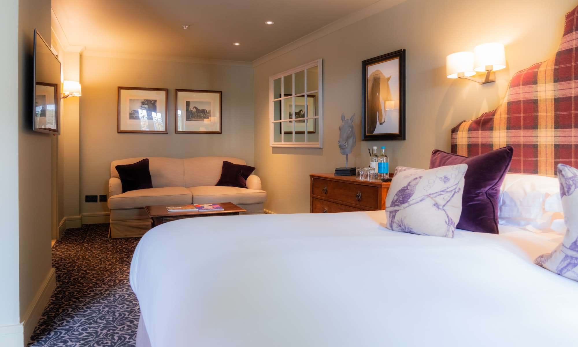 A bright hotel bedroom with a plaid headboard and mirrored wardrobe.