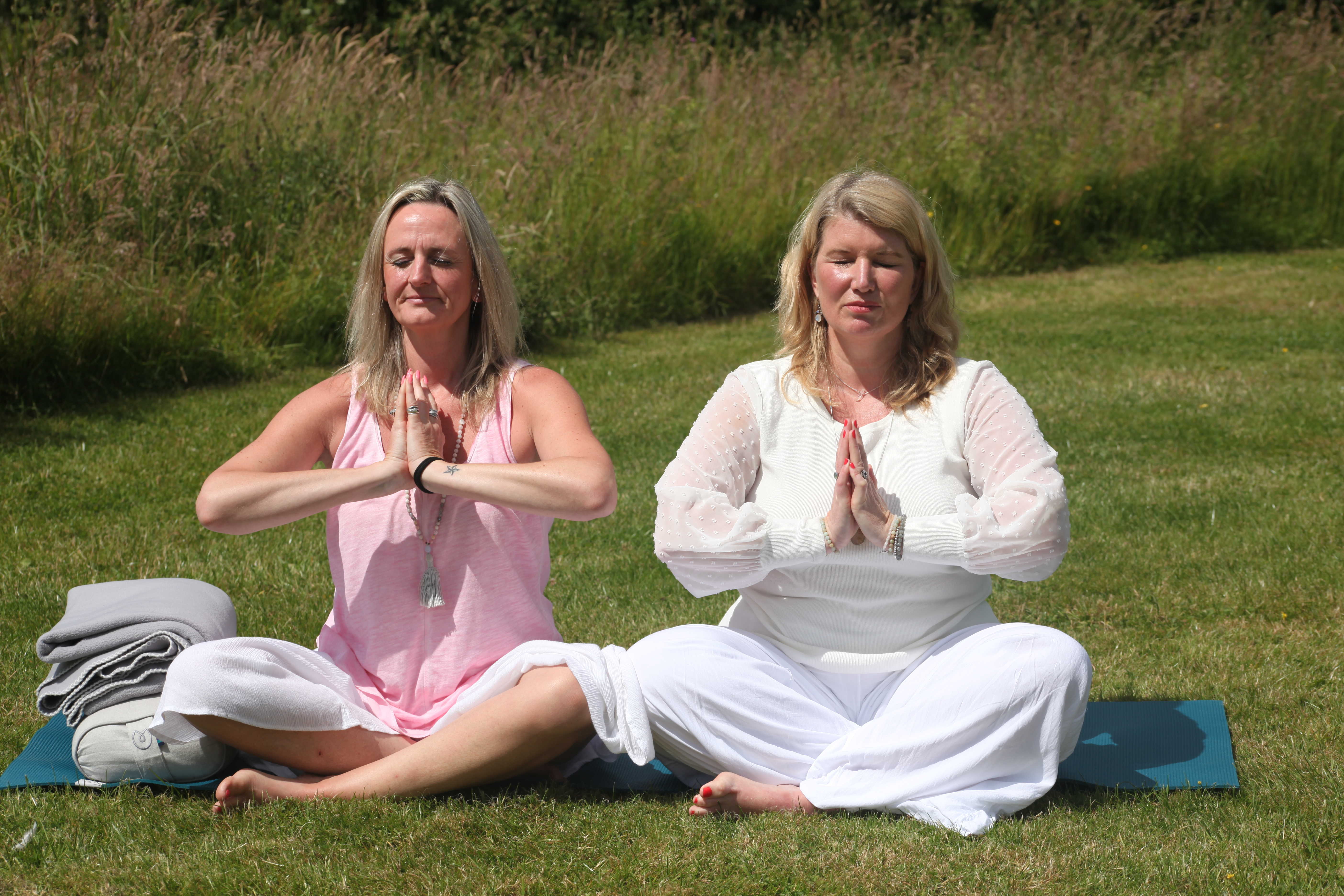 Two women meditating outdoors on grass.