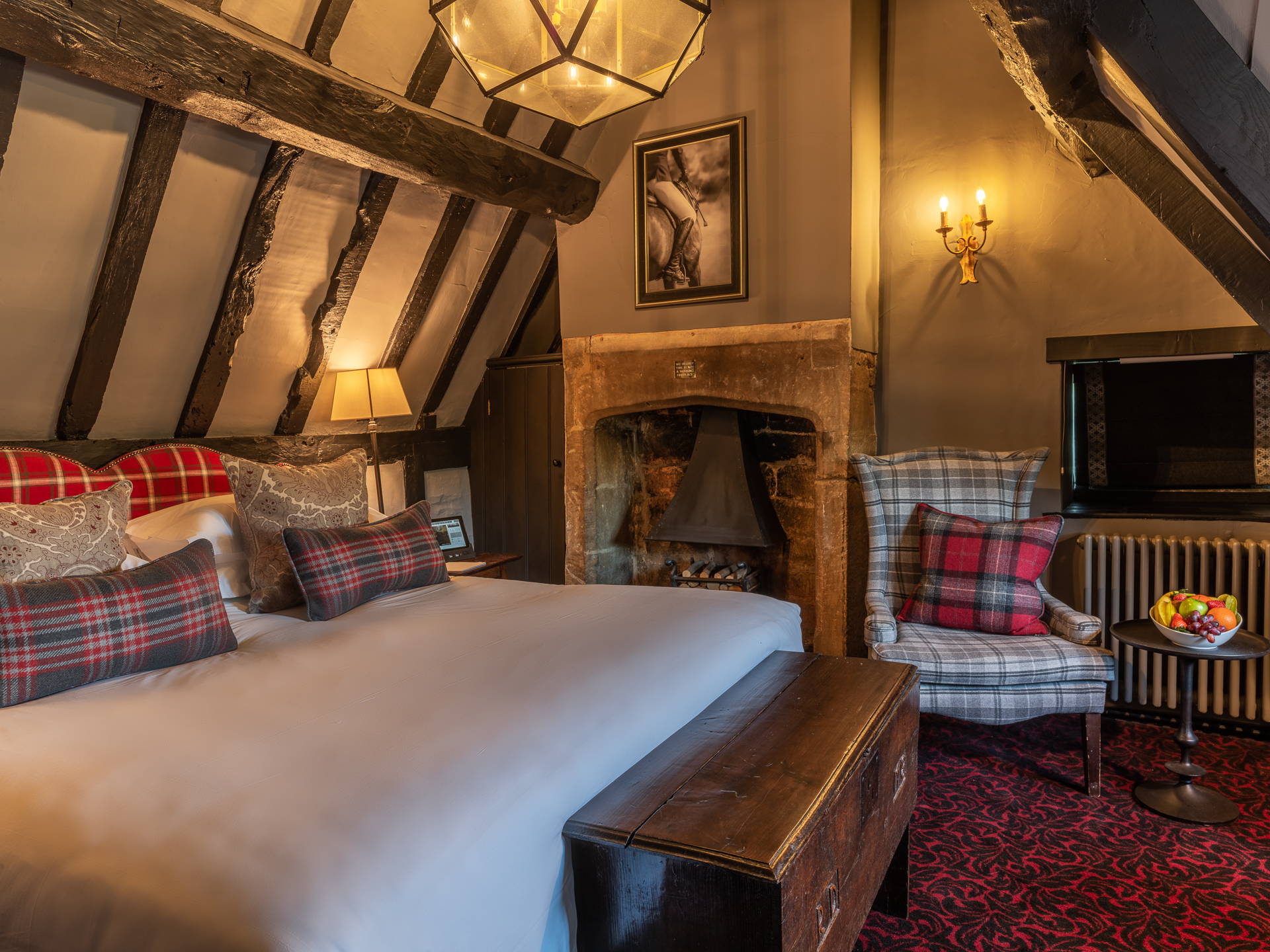 A rustic attic-style room with exposed beams, fireplace, and plaid accents.