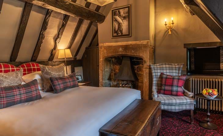 A rustic attic-style room with exposed beams, fireplace, and plaid accents.