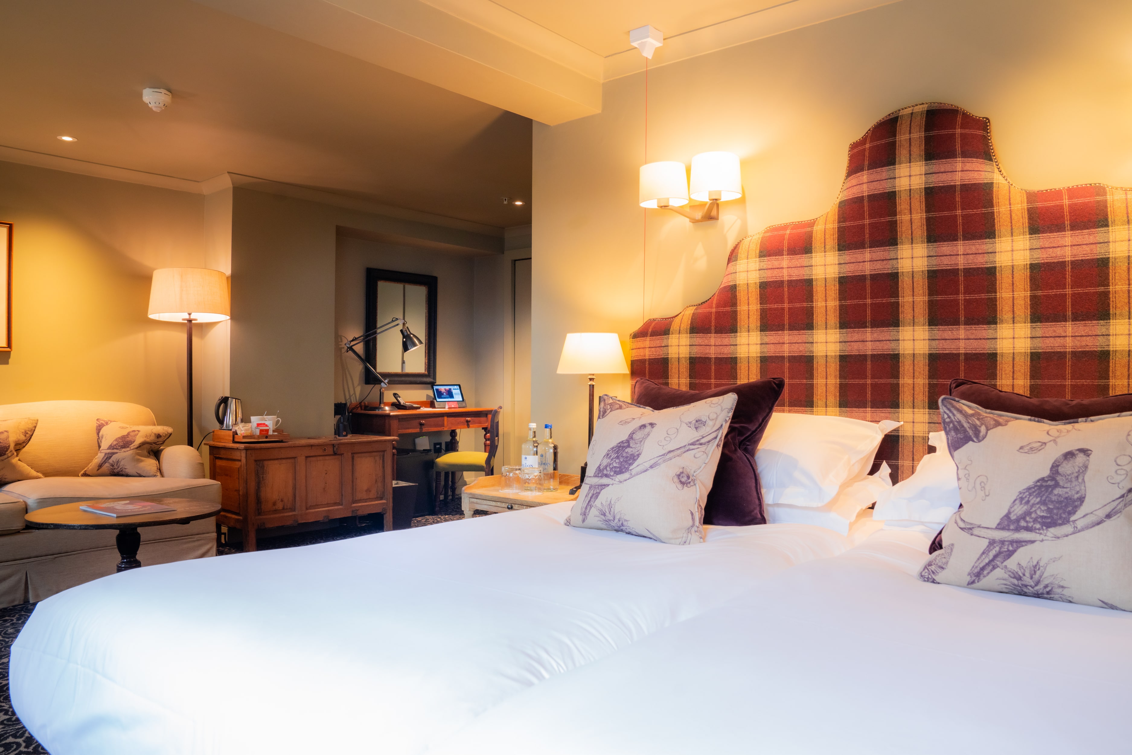 A cosy hotel room with sofa, desk, and plaid headboard.