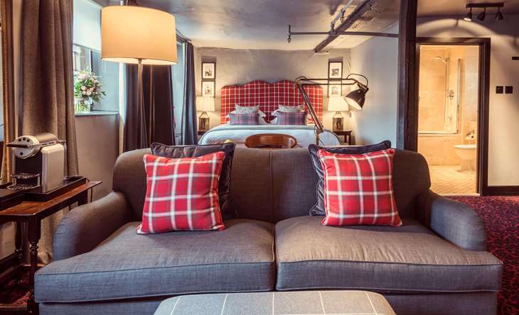 A warm attic-style room with exposed beams, a sofa, and an open bathroom door.