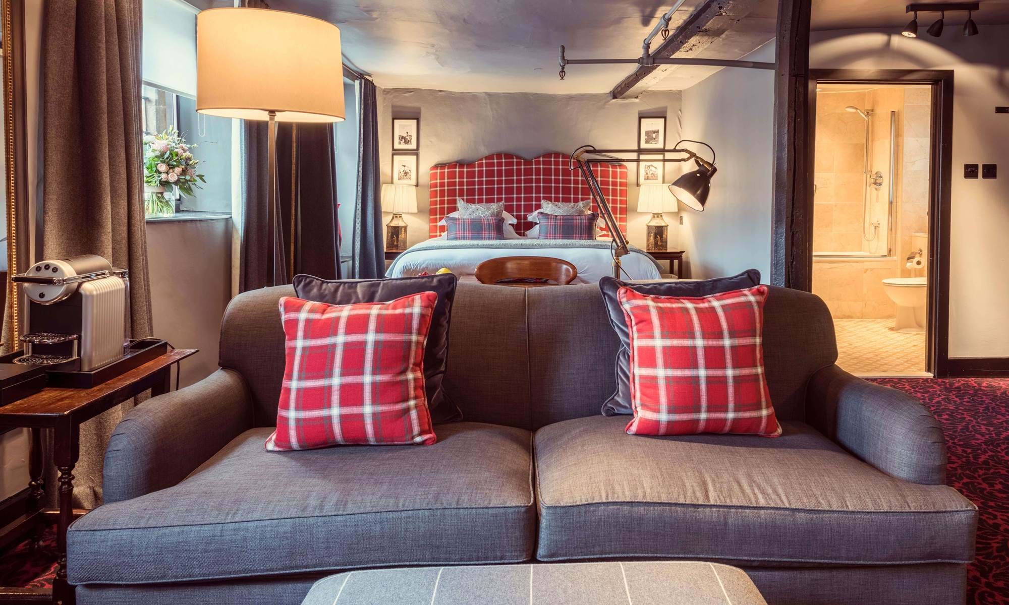 A warm attic-style room with exposed beams, a sofa, and an open bathroom door.