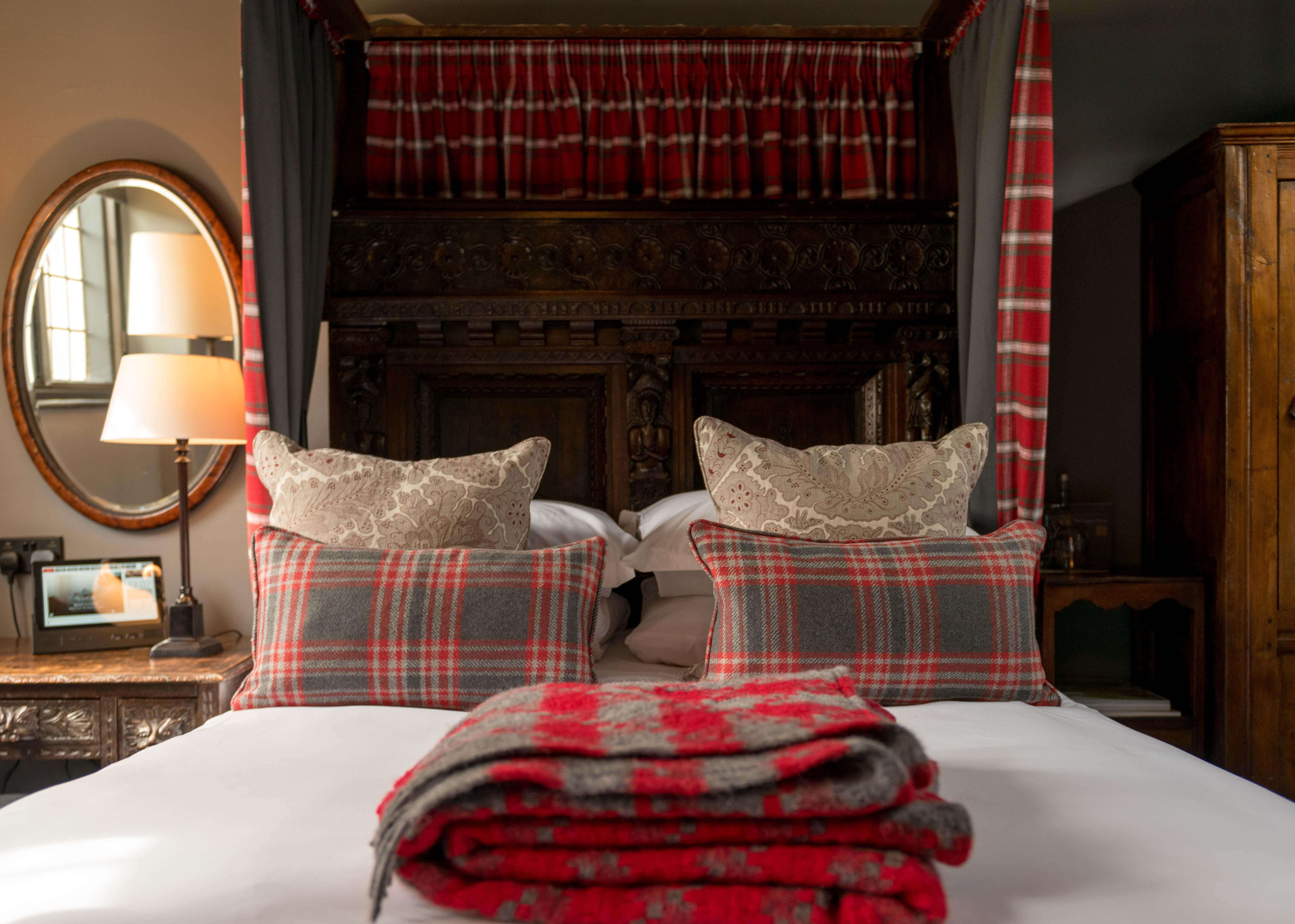 Traditional bedroom with plaid cushions, a four-poster bed, and a vintage nightstand with a lamp.