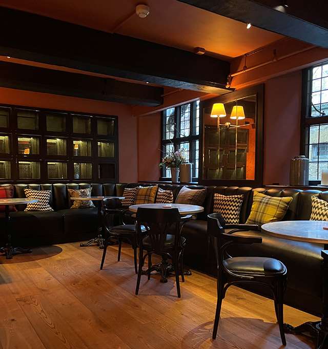 Cosy restaurant with black leather seating, patterned cushions, and round tables.