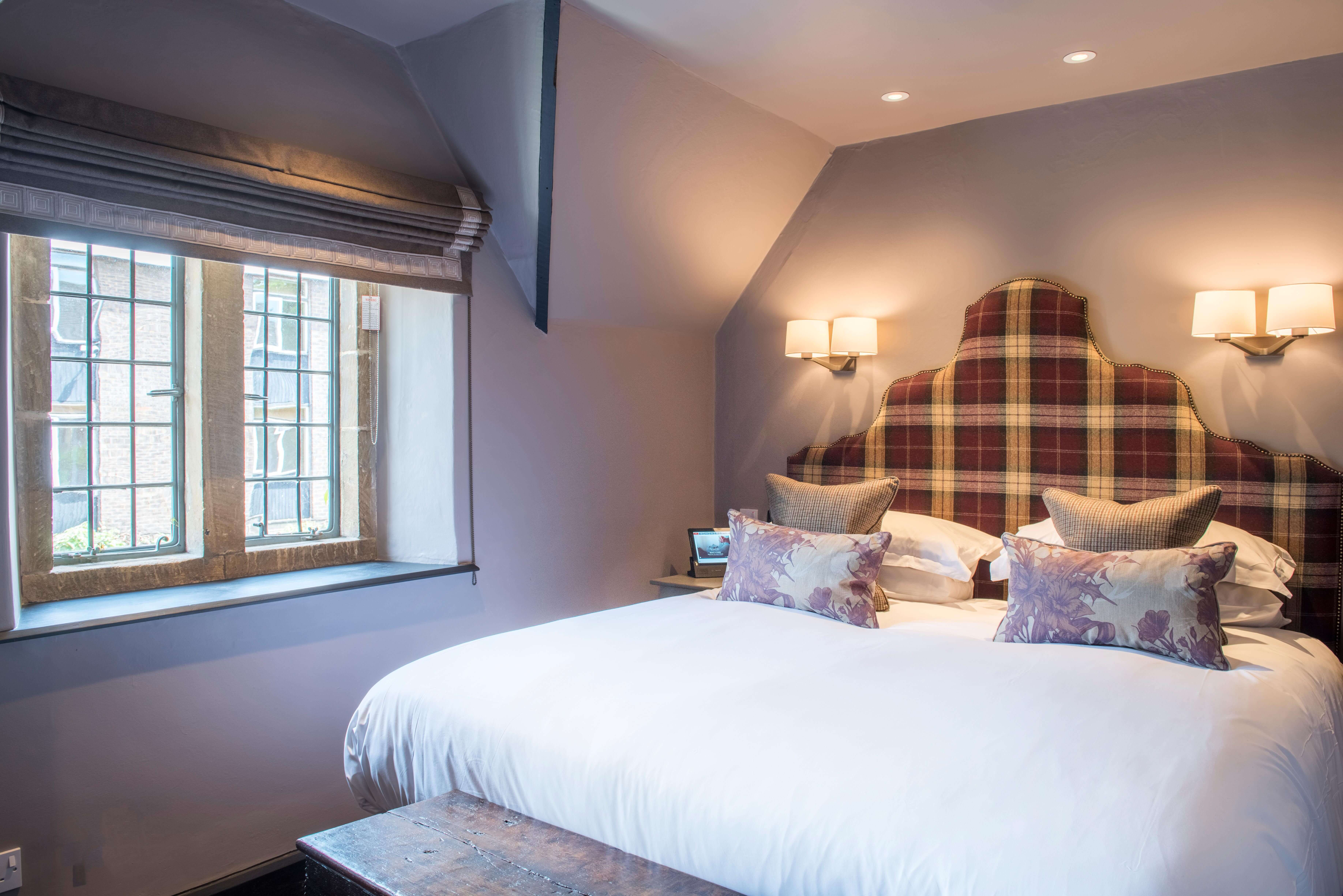 Cosy double bedroom with plaid headboard, soft lighting, and a window with roman blinds.