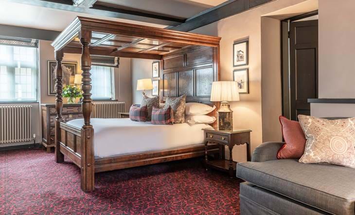 Bedroom with plaid accents, armchair, and four posters wood bed.