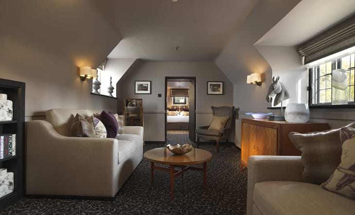 A stylish hotel lounge with sofas, armchairs, and a view into a bedroom.