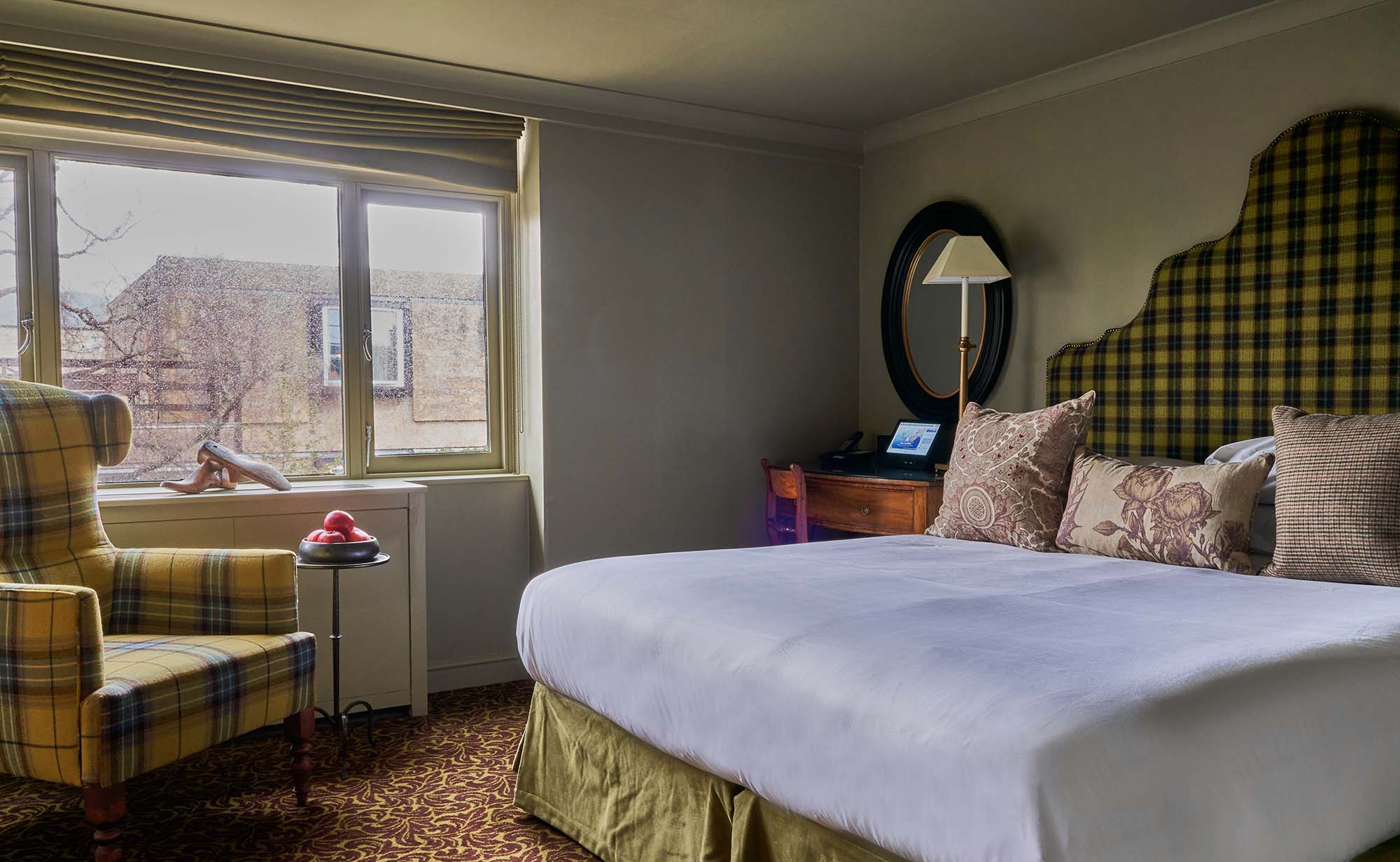 A cosy hotel room with yellow plaid accents, a lamp, and framed wall art.